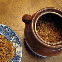 Boston baked beans in bean pot with blue plate with baked beans on the side.