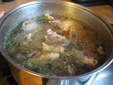 Pot of water simmering on the stove with chicken carcass and herbs.