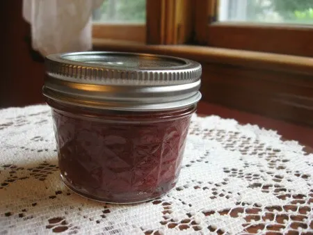 Jar of strawberry sauce on a table with a doily.