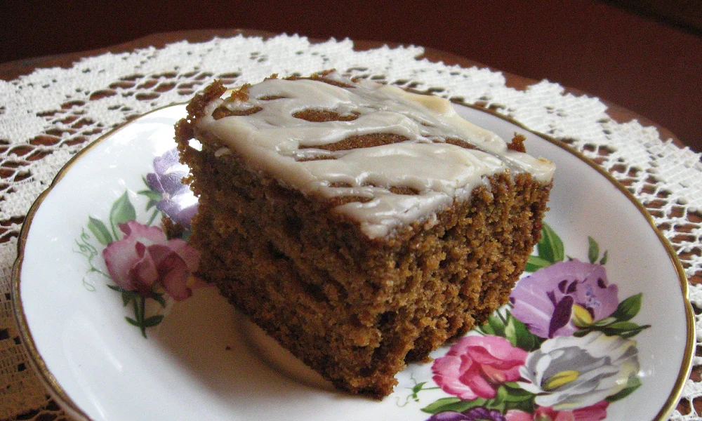 Slice of sour milk gingerbread with icing on a china plate with pink and purple flowers.