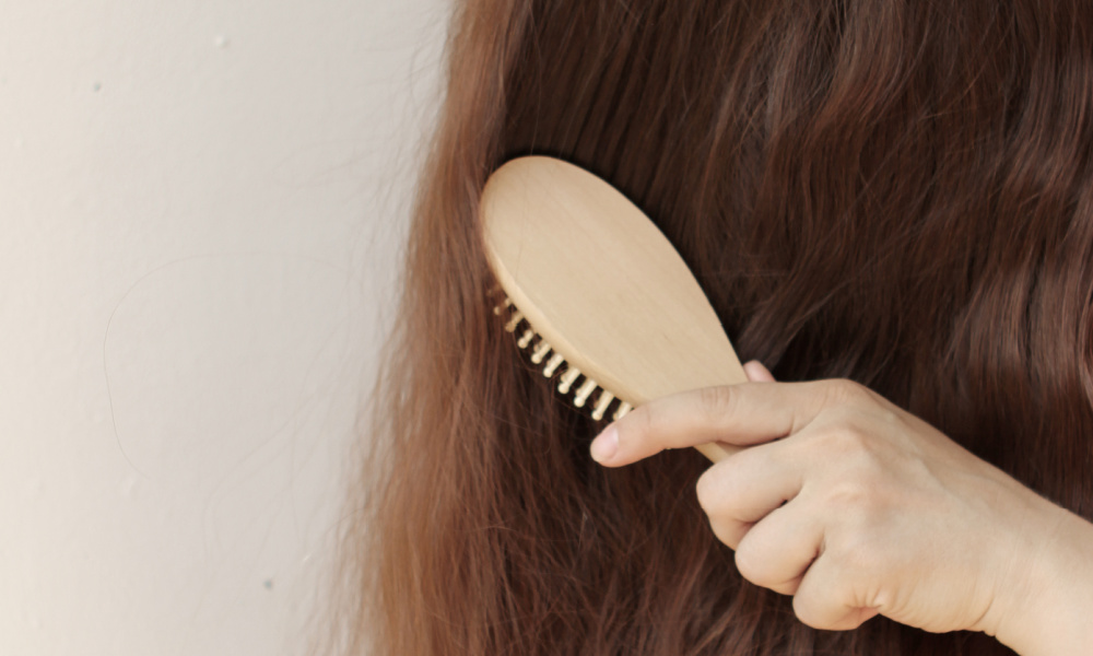 Hand holding hair brush and brushing long, brown hair.