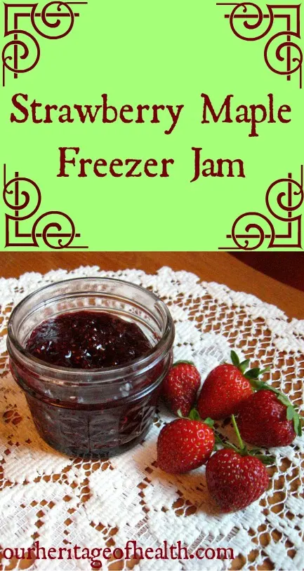 Glass jar of homemade maple-sweetened strawberry jam on a table with a lace doily with strawberries beside it.