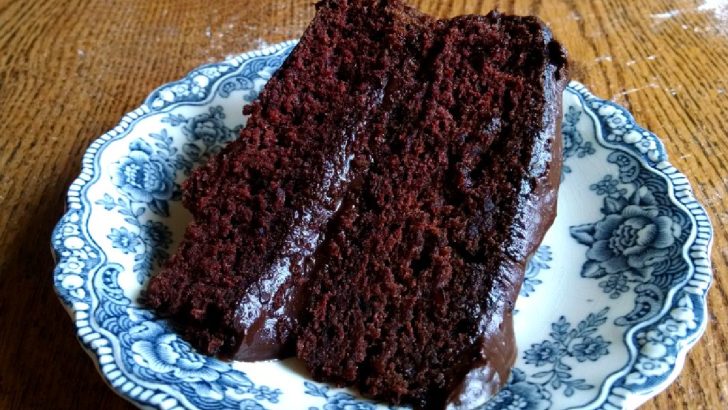 Slice of chocolate cake with chocolate frosting on a blue China plate.
