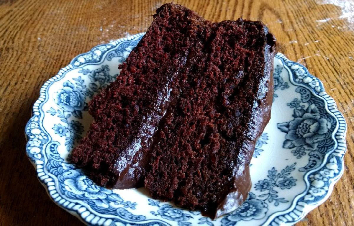 Slice of chocolate cake with chocolate frosting on a blue China plate.