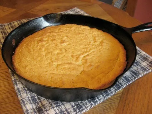 Cast iron skillet filled with cornbread on a blue and white checked cloth.