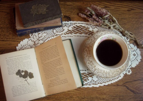 cup of tea with antique books and dried herbs and clover on table