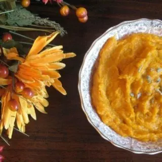 Bowl of mashed butternut squash with fall flowers beside it on a table.
