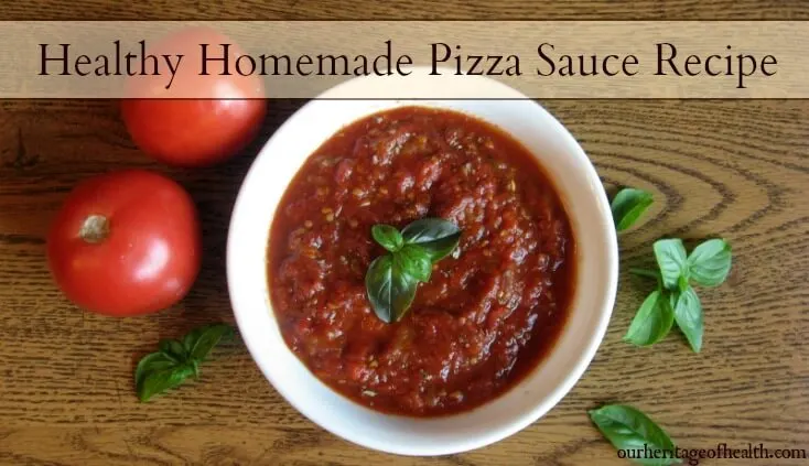 Bowl of homemade pizza sauce with basil and tomatoes on a table next to it.