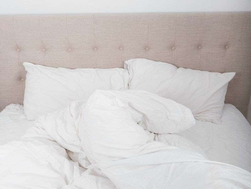 White pillows and crumpled sheets on a bed.