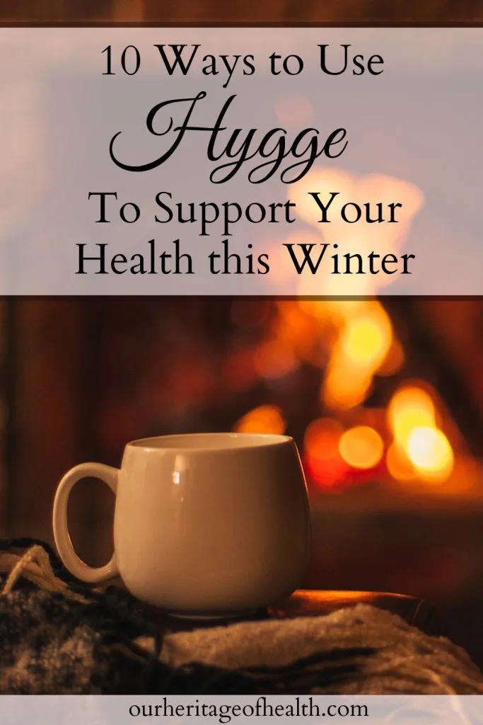 Mug on a table with a blanket next to it and a fireplace in the background and a text overlay that says "10 Ways to Use Hygge to Support Your Health this Winter."