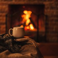 A mug and a blanket on a chair in front of a fireplace.