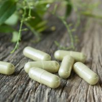 Supplement capsules on a wooden table with green leaves in the background.