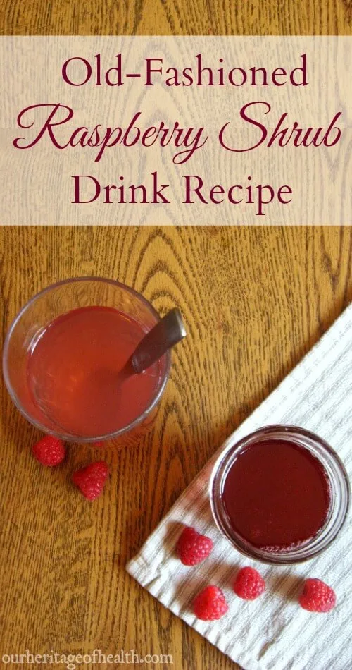 Mason jar of raspberry shrub next to a glass filled with water and shrub syrup with raspberries scattered around.