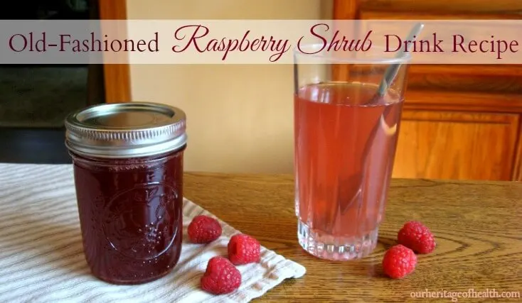 Mason jar of raspberry shrub next to a glass filled with water and shrub syrup with raspberries scattered around.