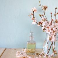 Bottle of perfume on a table next to pink flowers with a pale blue background.