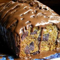 Loaf of chocolate chip pumpkin bread on a blue plate with chocolate icing drizzled over it.