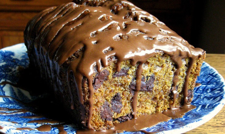 Loaf of chocolate chip pumpkin bread on a blue plate with chocolate icing drizzled over it.