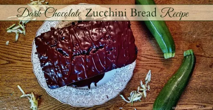 Loaf of zucchini bread with chocolate glaze on a plate with two zucchinis beside it.