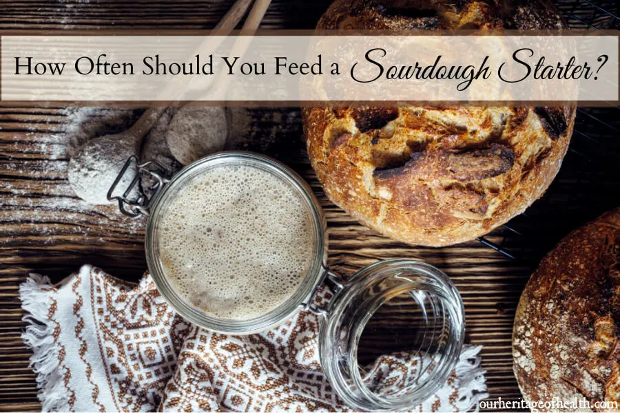 Jar of sourdough starter on table with loaf of bread and baking utensils.