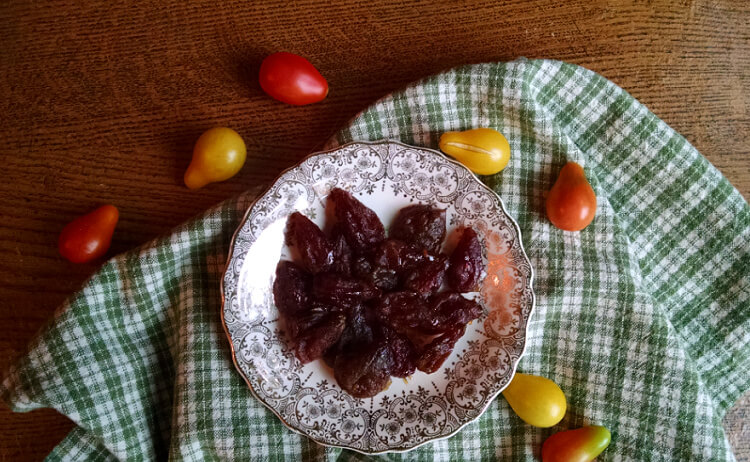 Dried tomatoes on plate with green checked cloth and small pear-shaped tomatoes scattered around.