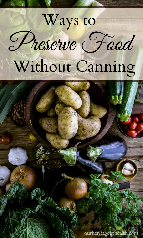 A variety of fresh vegetables and herbs on a wooden table including potatoes, cabbage, oregano, onions, garlic, lettuce, tomatoes, etc.