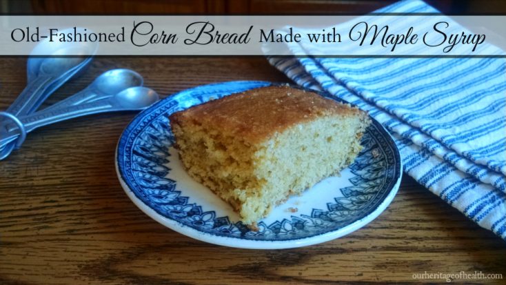 Square slice of corn bread on a blue and white china plate on a table with measuring spoons and a blue and white striped towel beside it.