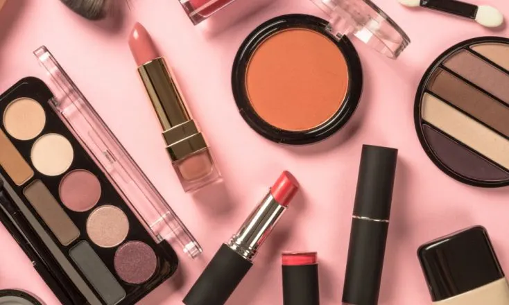 Lipstick, eye shadow, and blush containers scattered on a pink background.