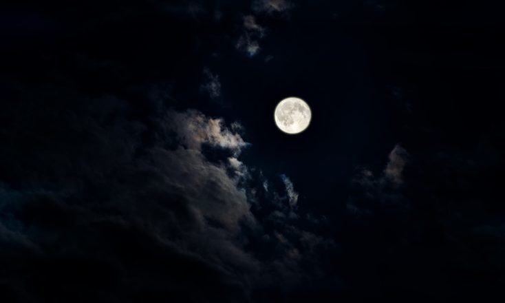 Full moon in the night sky with moonlit clouds.