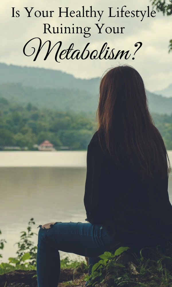 Woman facing away from the camera sitting on the shore of a lake looking out at the water and the hills in the background.