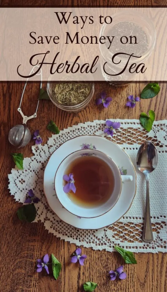 Tea cup on a lace doily with a spoon beside it and glass jars full of herbs and a tea infuser on a table with violet flowers and leaves scattered around.