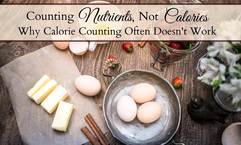 Table with ingredients scattered on it including butter, eggs, cinnamon sticks, and strawberries and a decorative bird figurine and flowers beside them and text overlays that said "Counting Nutrients, Not Calories" and "Why Calorie Counting Often Doesn't Work."