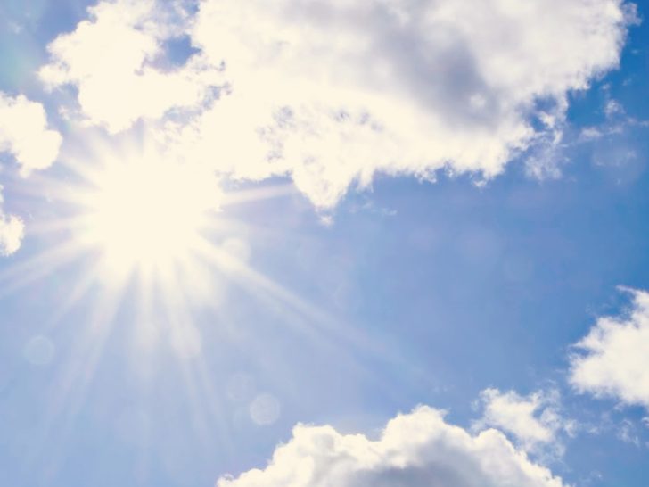 Sun shining through the clouds in a bright blue sky.