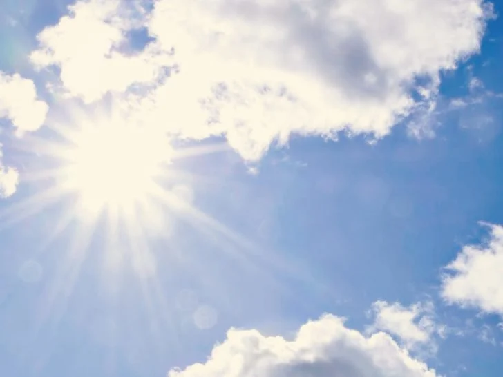 Sun shining through the clouds in a bright blue sky.