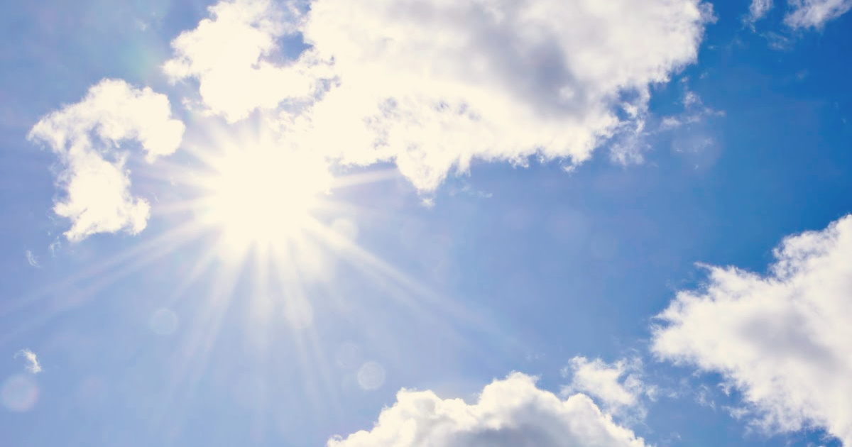 Sun shining through the clouds in a bright blue sky.