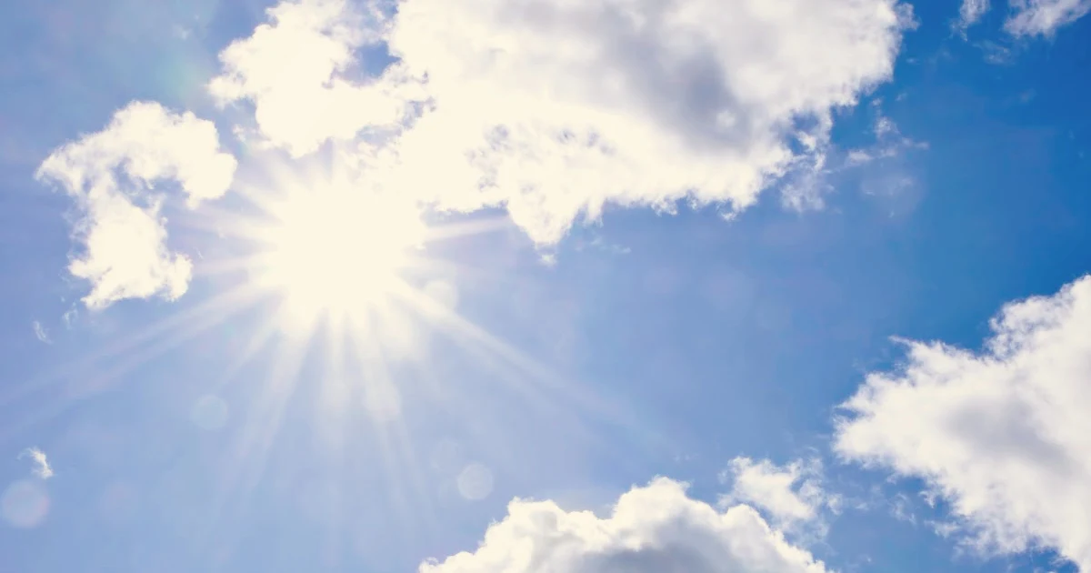 Sun shining through the clouds in a bright blue sky.