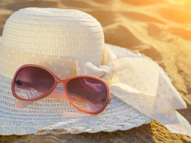 Pair of sunglasses sitting on top of a white sun hat on a beach with the glow of the sunshine.